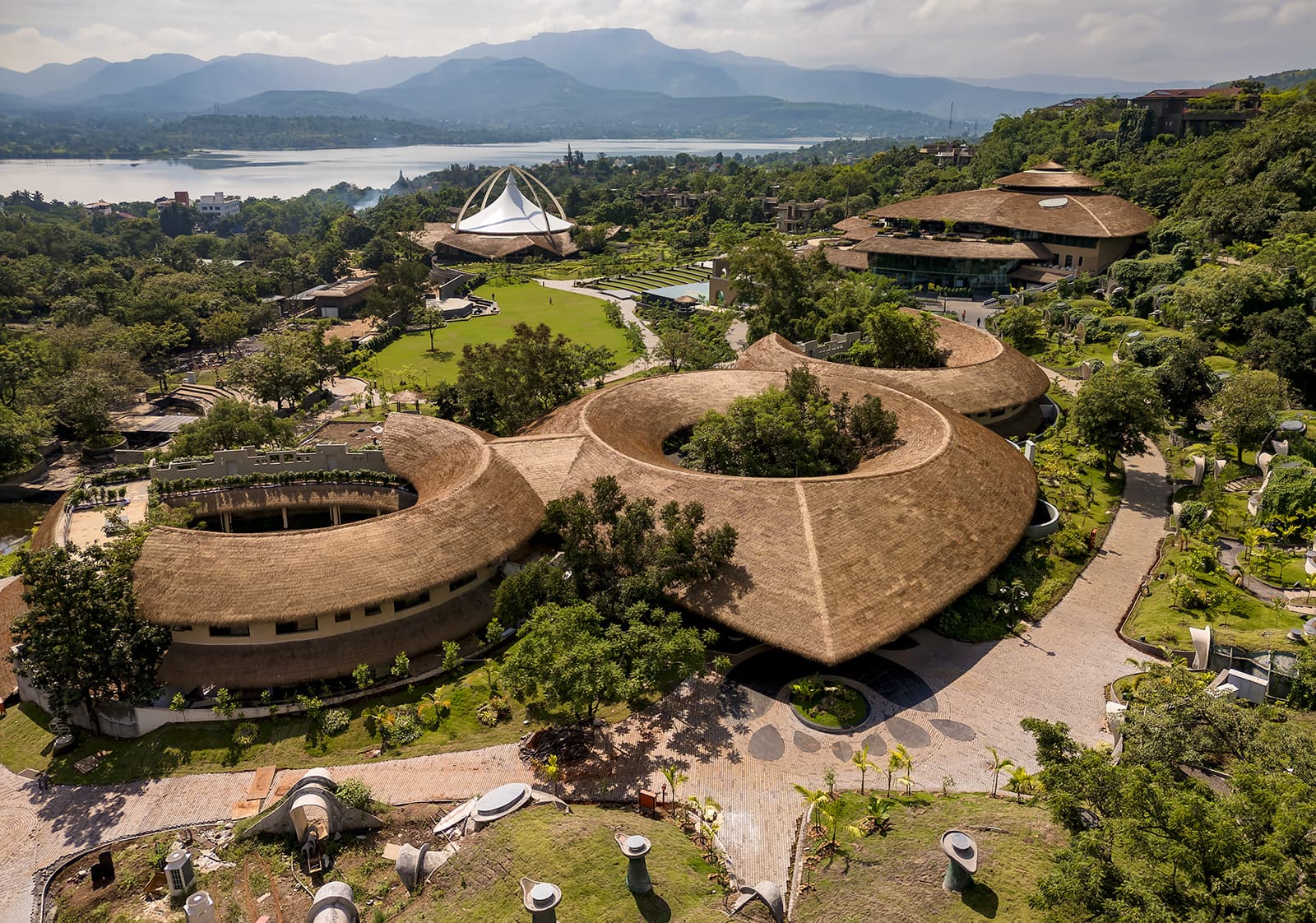 Ayu Vihar, near Mumbai, showcasing thatched circular buildings and lush greenery, known for luxury Ayurveda therapies.