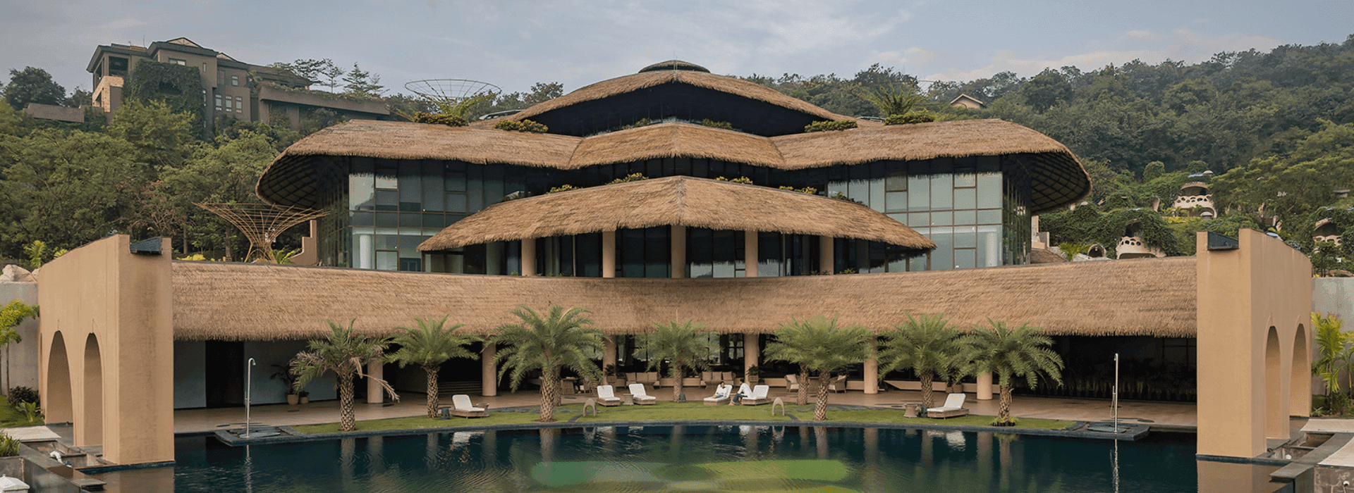 Anand Vihar's serene exterior with thatched roofs, pool, and greenery at a luxury health and wellness retreat.