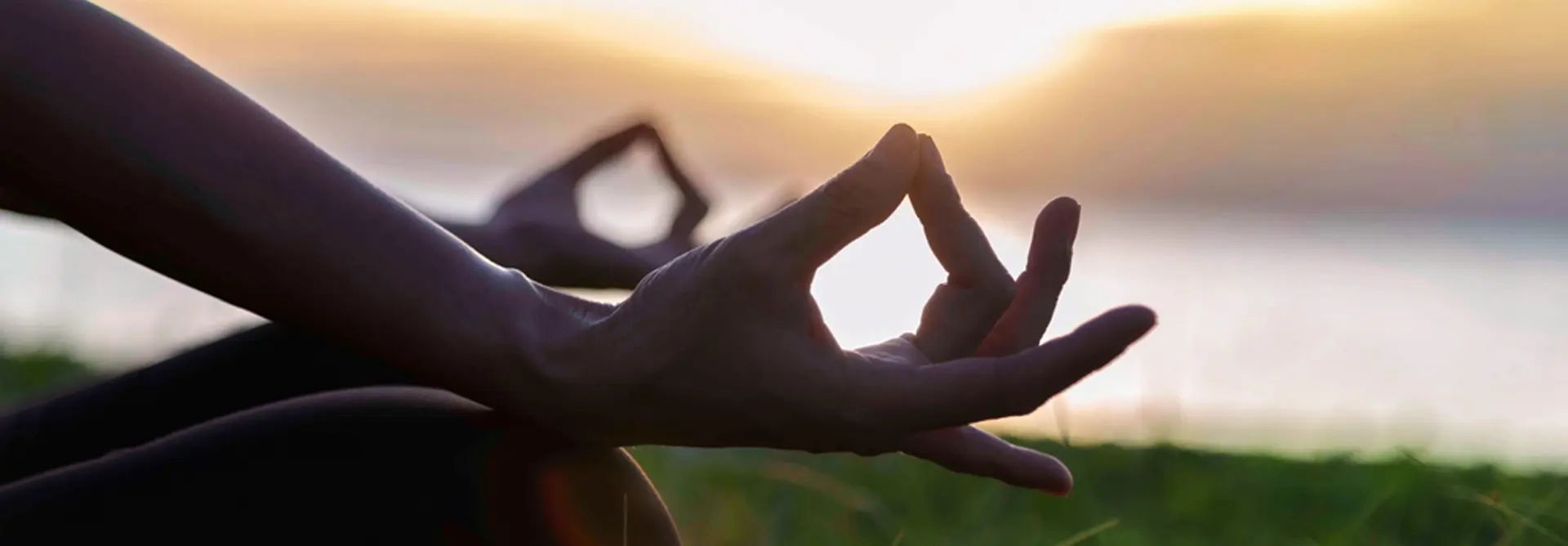 Hands in meditation pose during sunset, embodying holistic detox at Swastik Wellbeing's Ayurvedic programs near Pune.