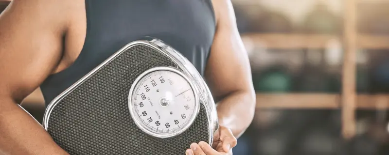 Person holding scale, symbolizing weight management in Swastik's Optimal Body Balance program, wellness weight loss center.