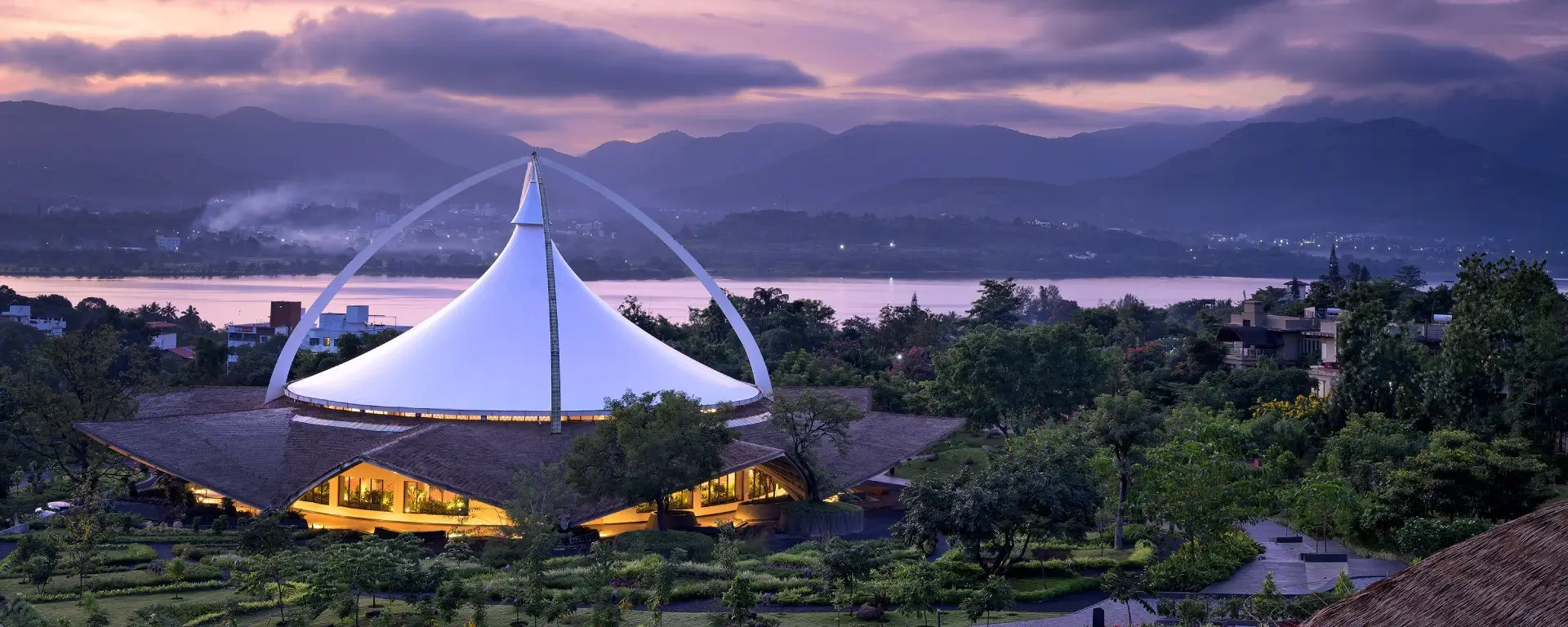 A large, column-less dome at Dhyan Vihar, set against mountains and a lake, offers guided meditation near Mumbai & Pune.