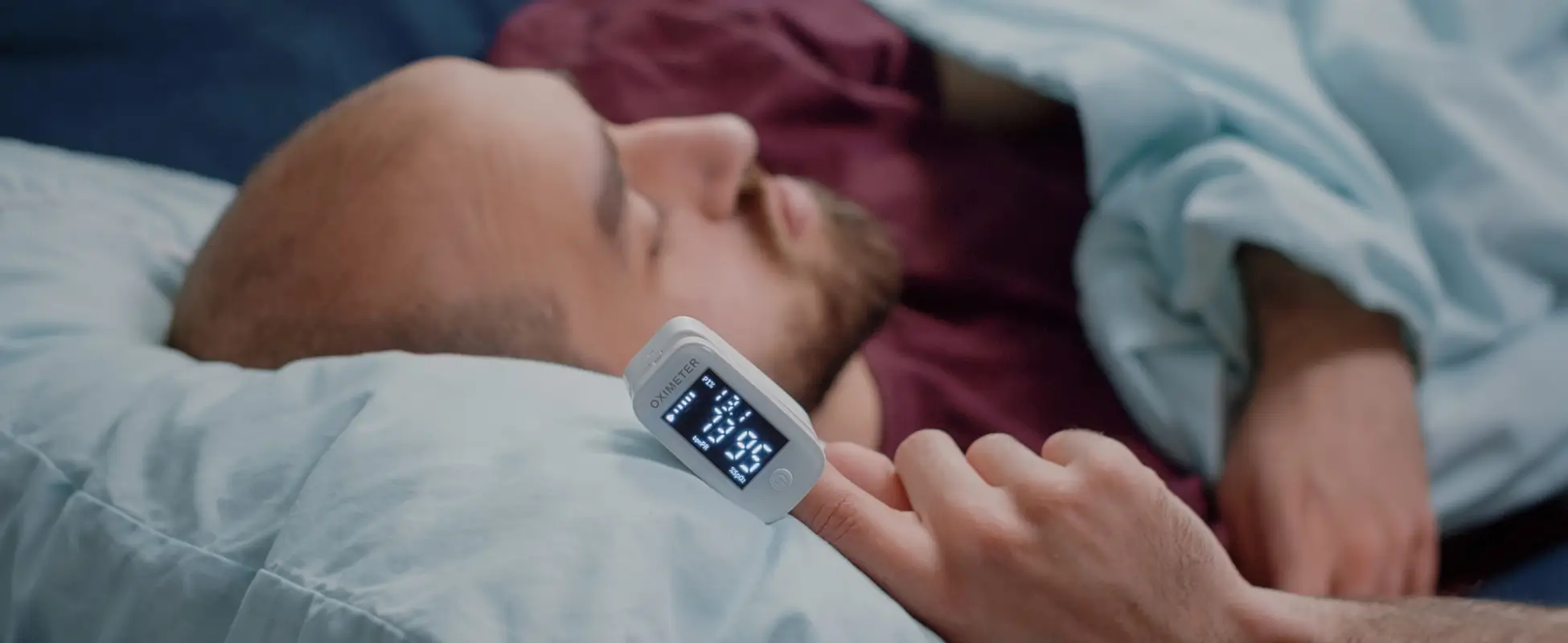 Man asleep in bed wearing a fingertip pulse oximeter during overnight sleep monitoring