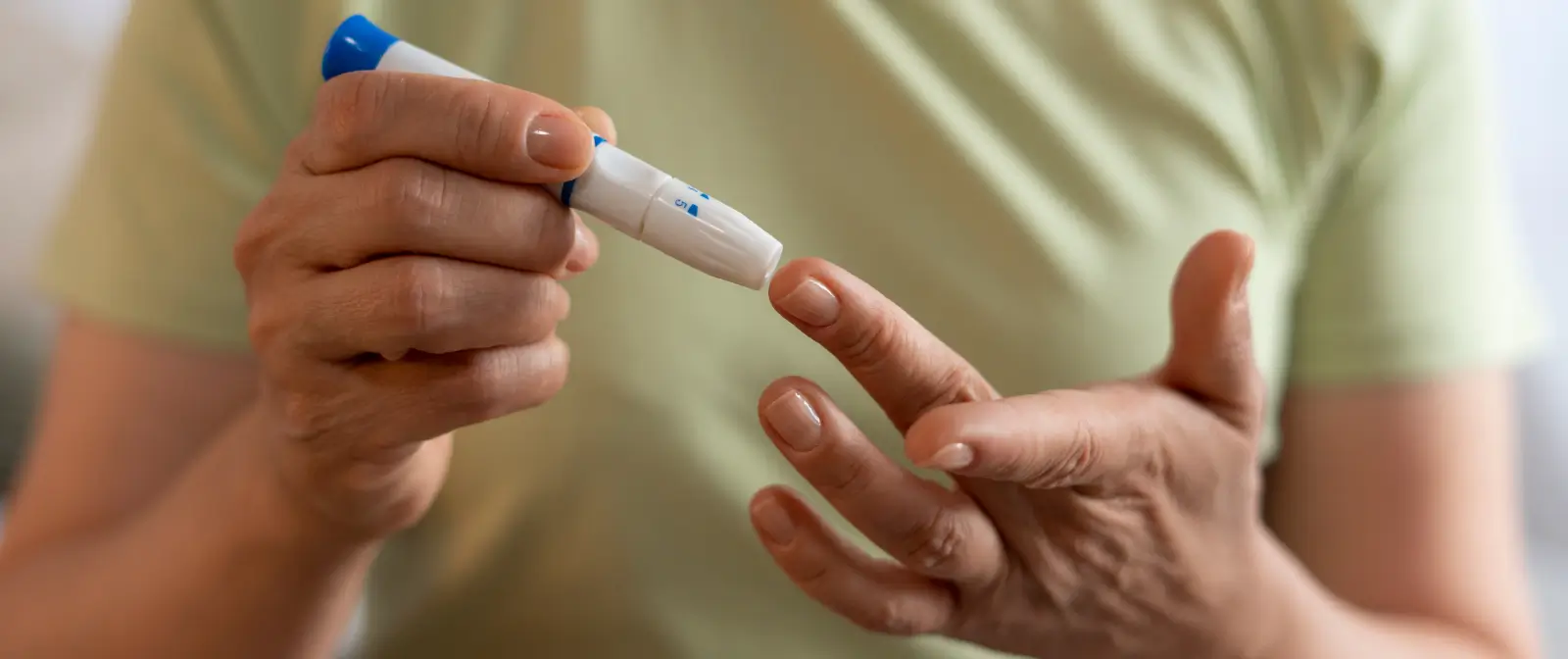 Insulin Resistance and Insulin Sensitivity_desk Hands using a lancet pen to check blood sugar, which insulin resistance slowly disrupts